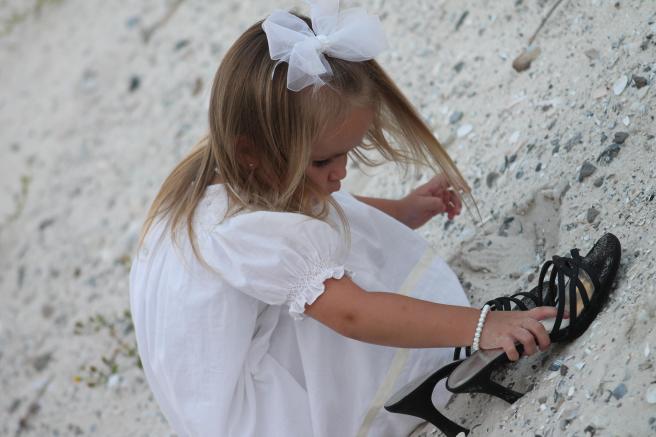 child at beach with mom's shoes