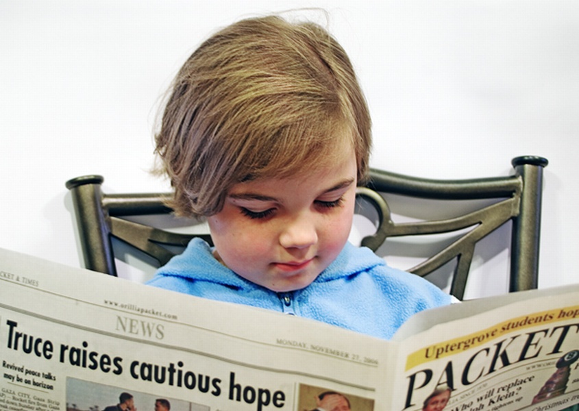 A young girl reading the current events in a newspaper; isolated on white background.